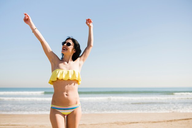 Retrato de una mujer joven sonriente en bikini de pie cerca del mar contra el cielo azul en la playa