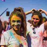 Foto gratuita retrato de una mujer joven sonriente con colores holi en su cara mirando a cámara