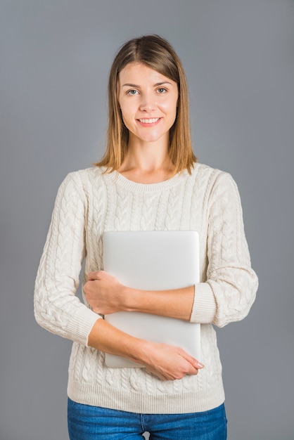 Retrato de una mujer joven sonriente con la computadora portátil en fondo gris