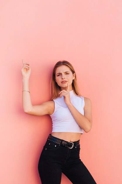 Retrato de una mujer joven sonriente con el dedo en su barbilla que señala el dedo contra fondo del melocotón