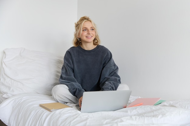 Retrato de una mujer joven sonriente estudiando en su cama trabajando desde casa en el dormitorio sentada con una computadora portátil