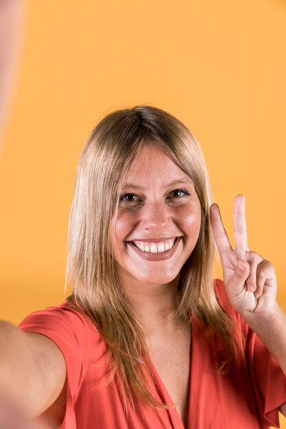 Retrato de mujer joven sonriente mostrando el signo de paz