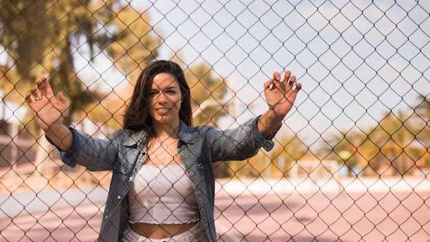 Foto gratuita retrato de una mujer joven sonriente de pie detrás de la valla