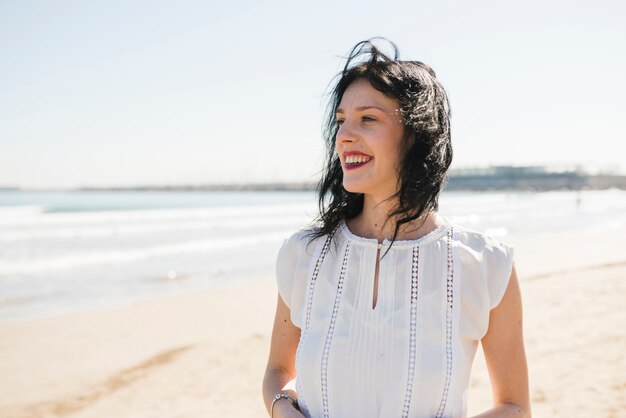 Retrato de una mujer joven sonriente que se coloca cerca del mar en la playa