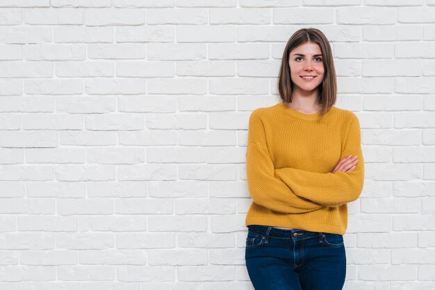 Retrato de una mujer joven sonriente que se opone a la pared blanca que mira la cámara