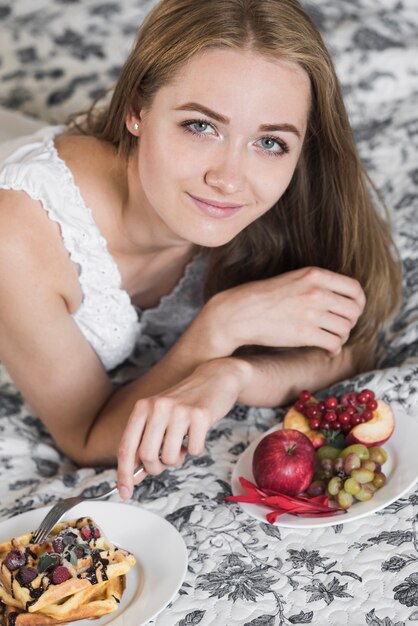 Retrato de la mujer joven sonriente que pone la bifurcación en la galleta