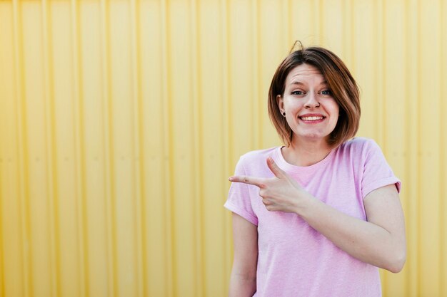 Retrato de una mujer joven sonriente que señala el dedo contra la hoja de metal amarilla acanalada