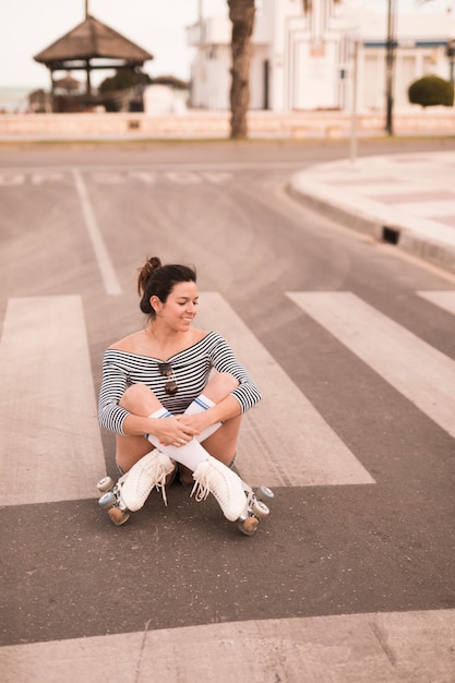 Retrato de una mujer joven sonriente que se sienta en el camino con sus piernas cruzadas que miran lejos