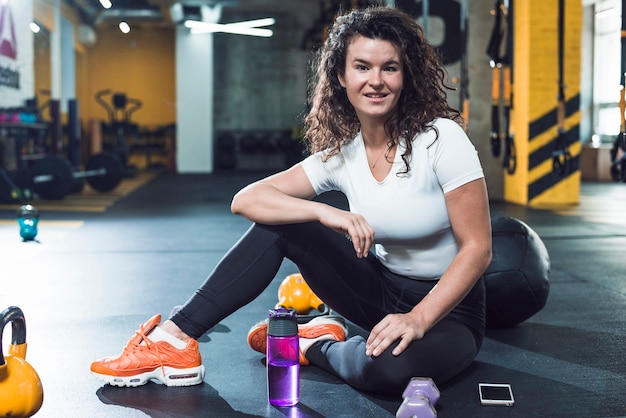 Retrato de una mujer joven sonriente que se sienta en piso en gimnasio