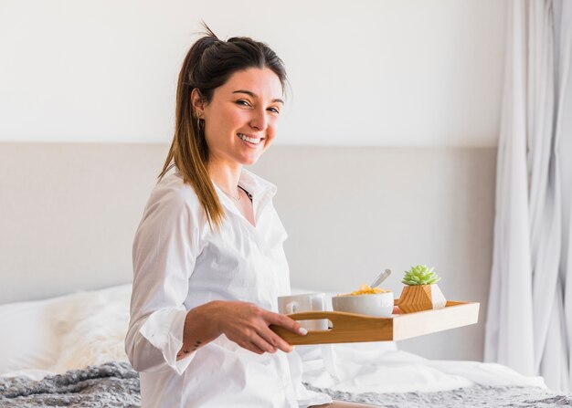 Retrato de una mujer joven sonriente que sostiene la bandeja del desayuno