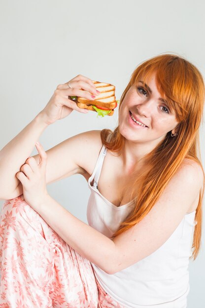 Retrato de la mujer joven sonriente que sostiene el bocadillo asado a la parrilla disponible