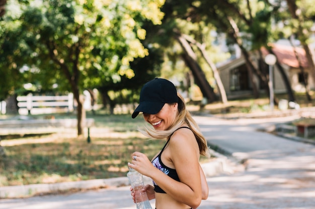 Foto gratuita retrato de la mujer joven sonriente que sostiene la botella de agua que se coloca en el parque