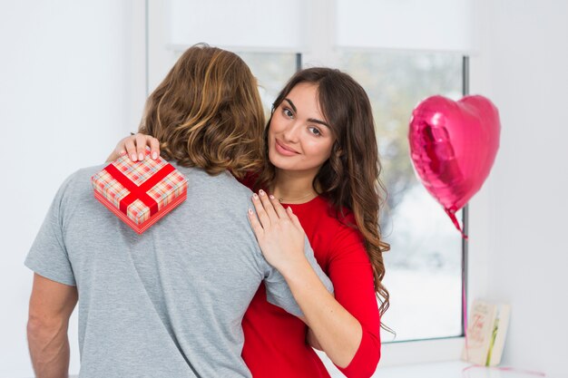 Retrato de una mujer joven sonriente que sostiene la caja de regalo roja que abraza a su novio