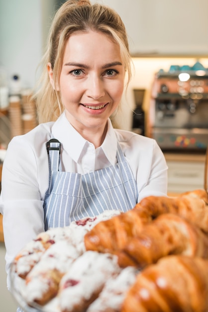 Retrato de una mujer joven sonriente que sostiene los croissants cocidos al horno frescos