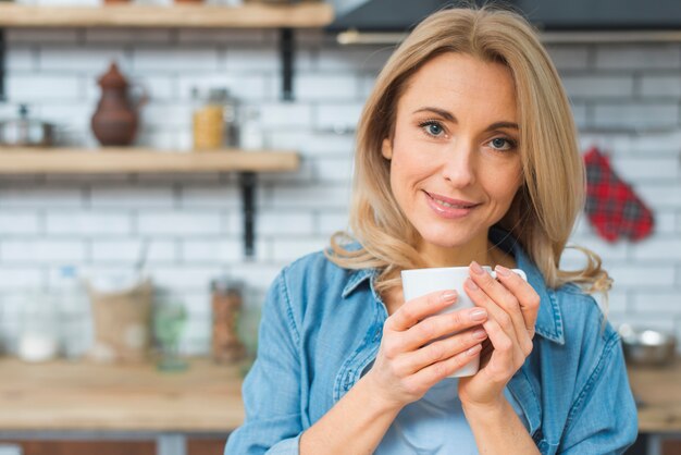 Retrato de una mujer joven sonriente que sostiene la taza de café blanca en la mano