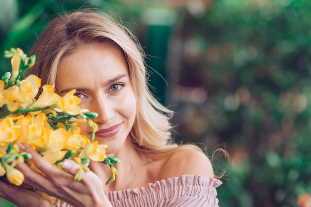 Retrato de una mujer joven sonriente que toca las flores amarillas de fresia con cuidado