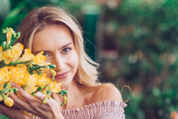 Retrato de una mujer joven sonriente que toca las flores amarillas de fresia con cuidado