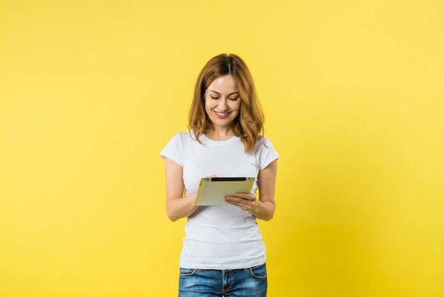 Retrato de una mujer joven sonriente que usa la tableta digital contra fondo amarillo