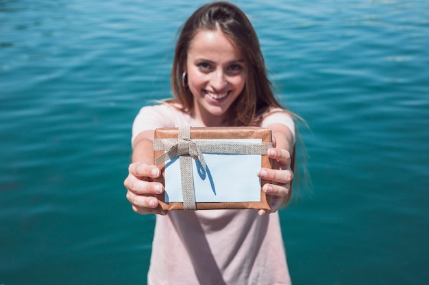 Foto gratuita retrato de una mujer joven sonriente con regalo frente al mar