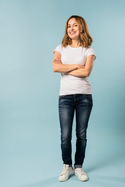 Retrato de una mujer joven sonriente con su brazo cruzado contra el fondo azul