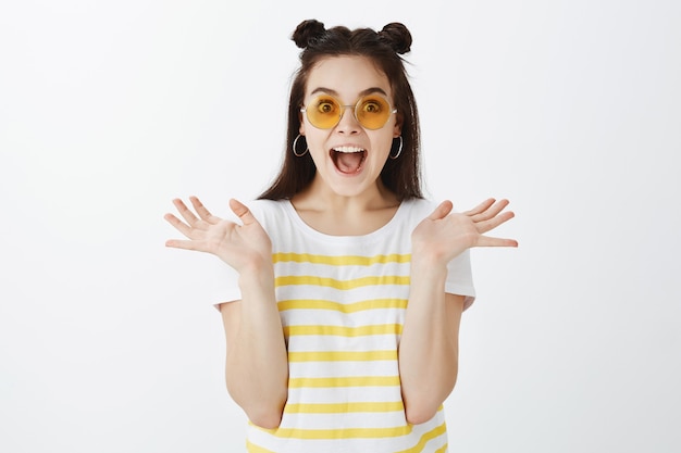 Retrato de mujer joven sorprendida posando con gafas de sol contra la pared blanca