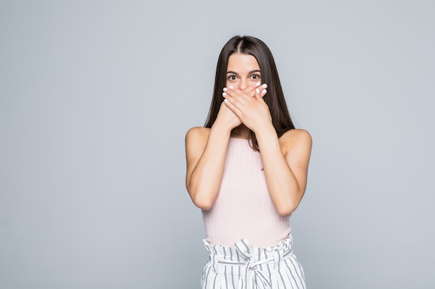 Foto gratuita retrato de una mujer joven sorprendida que cubre la boca con las manos aisladas sobre la pared blanca