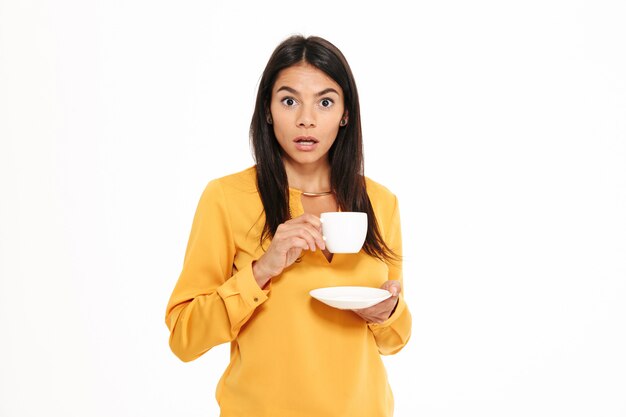 Retrato de una mujer joven sorprendida que sostiene la taza de té