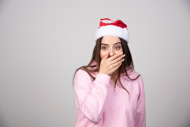 Retrato de una mujer joven sorprendida con sombrero de Santa cubriendo la boca con la mano.