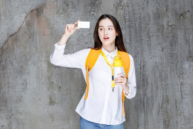 Retrato de mujer joven sosteniendo una botella de agua y mostrando la tarjeta de visita. foto de alta calidad