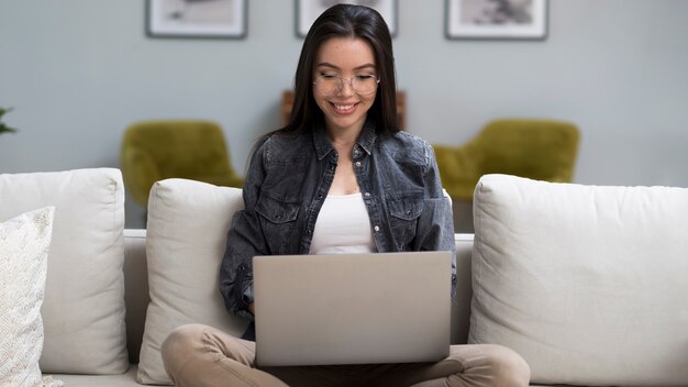 Retrato de mujer joven sosteniendo una computadora portátil en el sofá