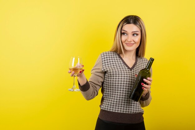 Retrato de mujer joven sosteniendo una copa y una botella de vino blanco.