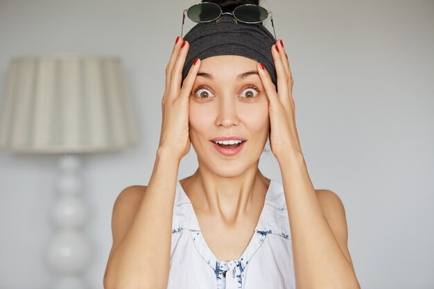 Retrato de mujer joven sosteniendo su cabeza con asombro con los ojos bien abiertos