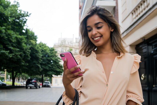 Retrato de mujer joven con su teléfono móvil mientras camina al aire libre en la calle