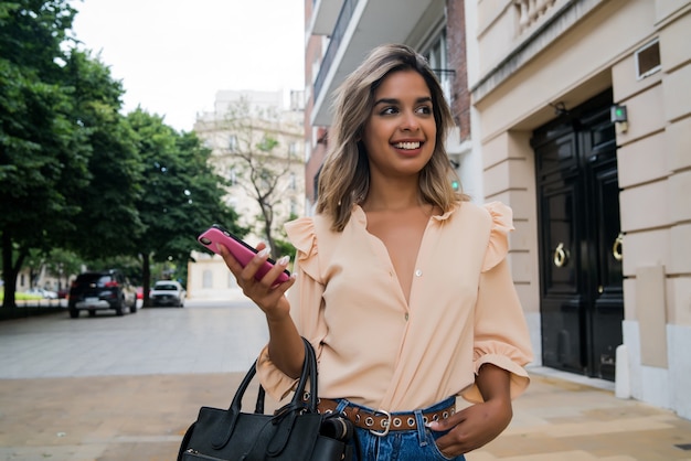 Retrato de mujer joven con su teléfono móvil mientras camina al aire libre en la calle