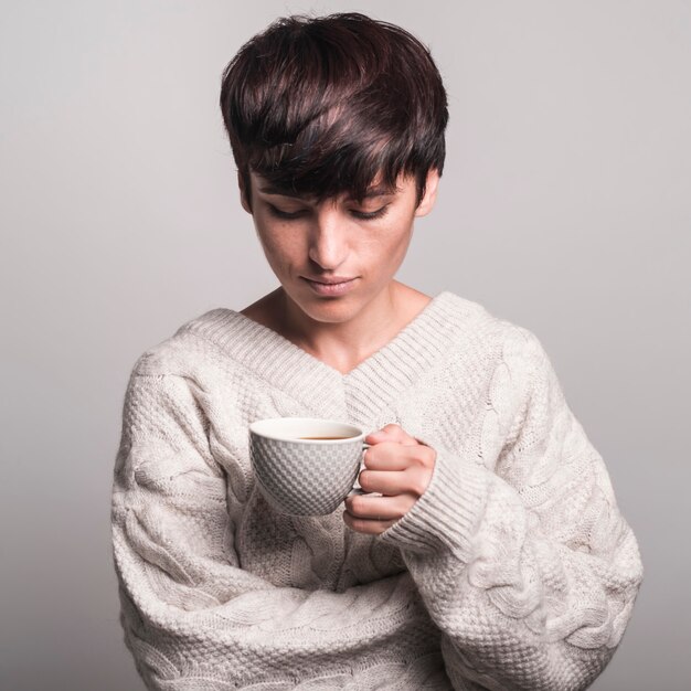 Retrato de mujer joven en suéter blanco mirando taza de café