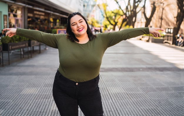 Foto gratuita retrato de mujer joven de talla grande sonriendo mientras está de pie al aire libre en la calle. concepto urbano.