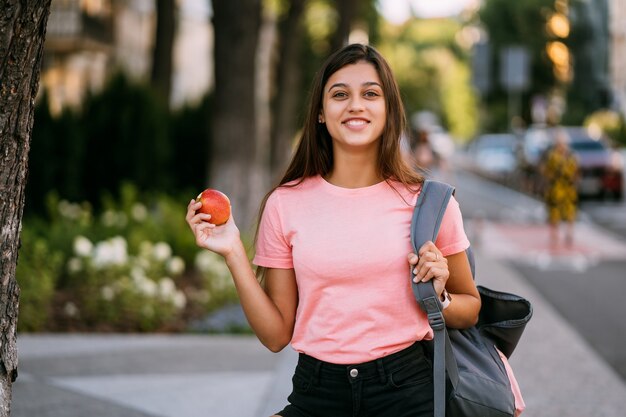 Retrato, de, un, mujer joven, tenencia, manzana, contra, un, calle, plano de fondo