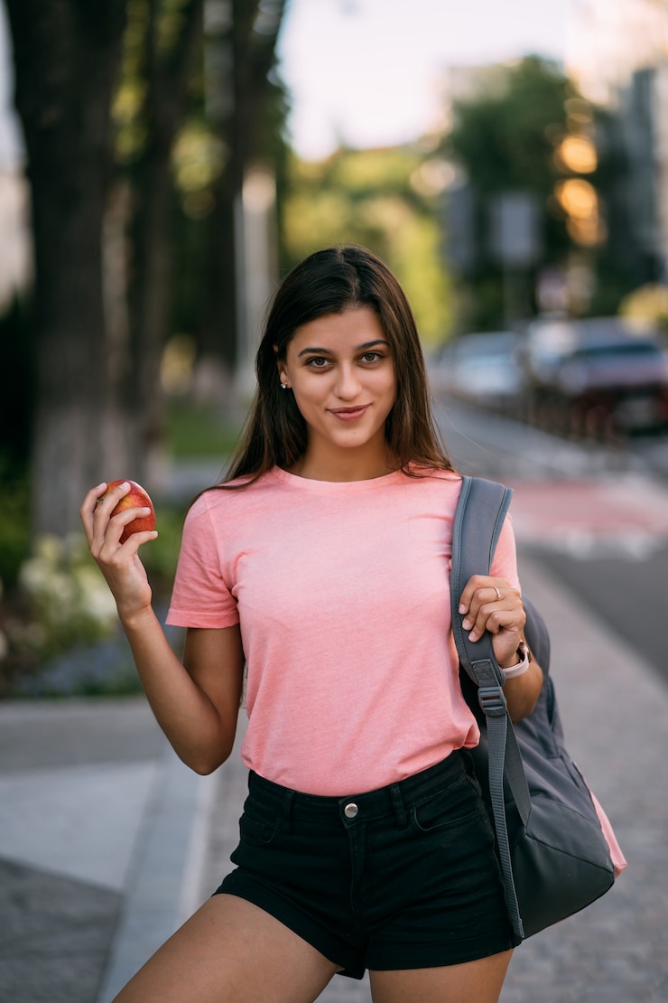 Foto gratuito retrato, de, un, mujer joven, tenencia, manzana, contra, un, calle, plano de fondo