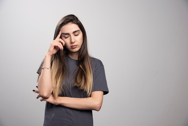 Retrato de mujer joven tocando su cabeza posando sobre fondo gris.