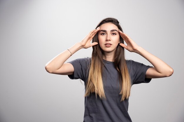 Retrato de mujer joven tocando su cabeza posando sobre fondo gris.