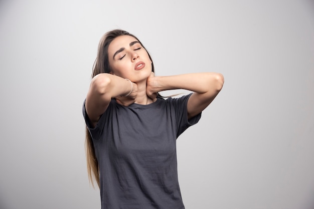 Retrato de mujer joven tocando su cuello posando sobre fondo gris.