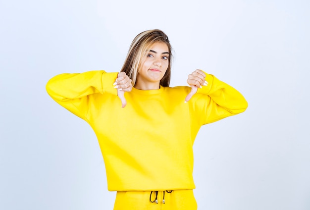 Retrato de mujer joven en traje amarillo dando pulgares hacia abajo