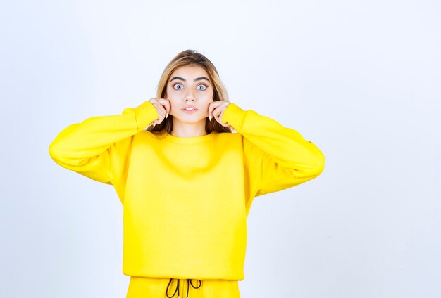 Retrato de mujer joven en traje amarillo de pie y posando sobre pared blanca