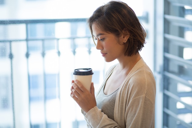 Retrato de la mujer joven tranquila que se coloca con la taza de café