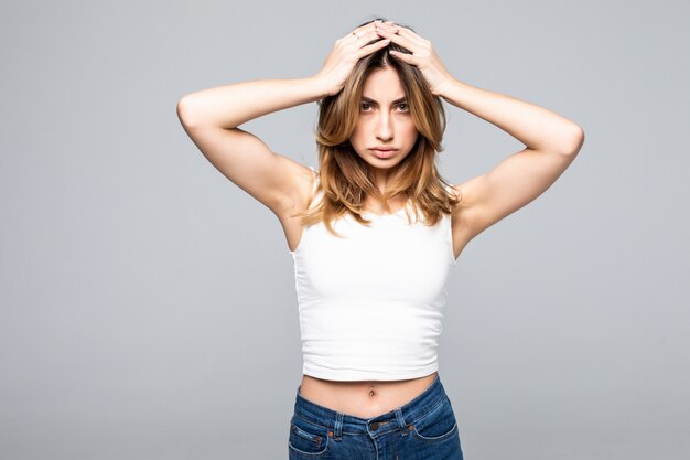 Retrato de mujer joven triste con las manos sobre la cabeza de pie sobre la pared gris