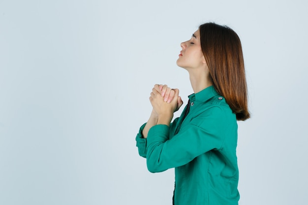 Foto gratuita retrato de mujer joven uniendo las manos en gesto de oración en camisa verde y mirando esperanzado