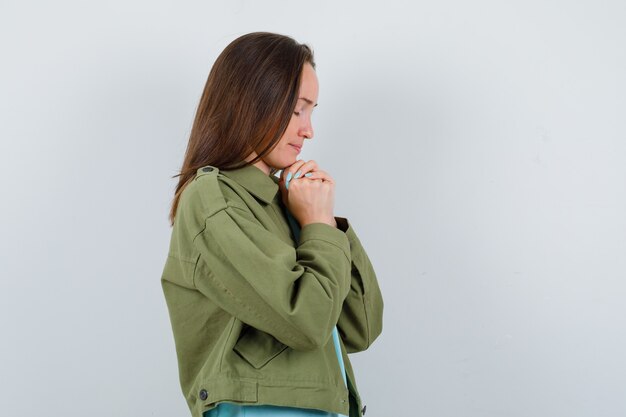 Retrato de mujer joven uniendo las manos en gesto de oración en chaqueta verde y mirando esperanzado