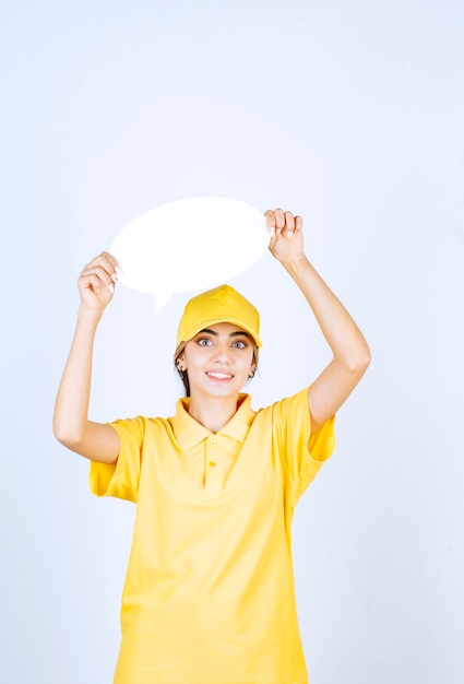 Retrato de una mujer joven en uniforme amarillo sosteniendo un bocadillo de diálogo en blanco vacío.