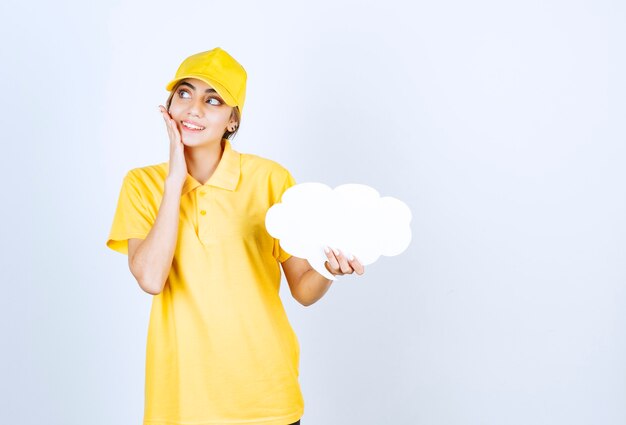 Retrato de una mujer joven en uniforme amarillo sosteniendo una nube de burbujas de discurso blanco vacío.