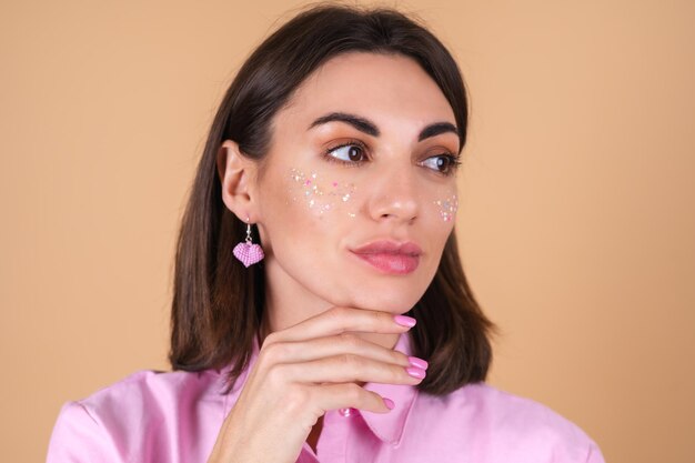 Retrato de una mujer joven con un vestido rosa con maquillaje de brillo brillante y lindos aretes posando positivamente